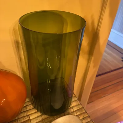 Tall, olive green glass cylindrical vase sitting on a cork-patterned surface.