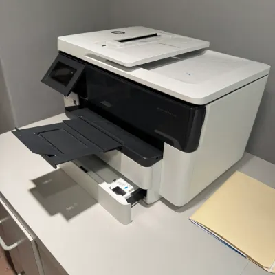 HP OfficeJet Pro all-in-one printer resting on a white office desk, featuring a top document feeder and extended output tray.