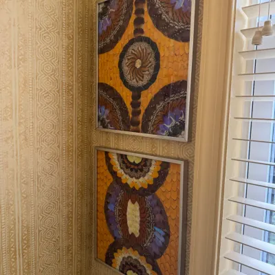 Pair of framed mid-century feather art collages with intricate geometric and mandala-inspired patterns in silver metal frames.
