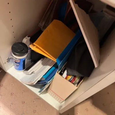 Assorted office and cleaning supplies, including notebooks, yellow envelopes, folders, and a tub of disinfectant wipes, stored inside a...
