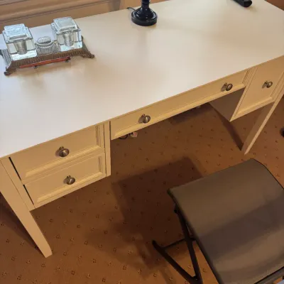 Off-white modern writing desk with multiple storage drawers, paired with a folding office chair and topped with a vintage glass inkwell set.