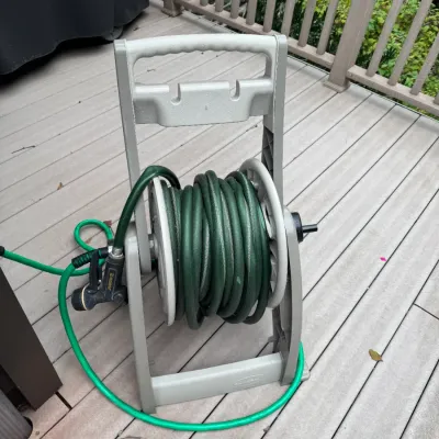 Suncast plastic garden hose reel stand with coiled green garden hose and attached Melnor spray nozzle.