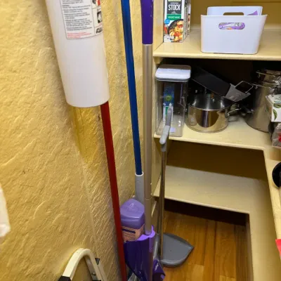 Pantry contents including a purple Swiffer WetJet, a fire extinguisher, long-handled dustpan, folding step stool, and kitchen cookware on...