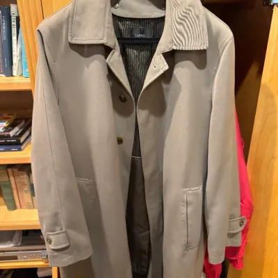 Men's Sanyo tan trench coat hanging on a Boyds Philadelphia hanger in a wooden closet cabinet.