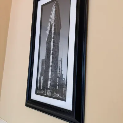 Framed black and white architectural photograph depicting the Flatiron Building in New York City, housed in a thick black wood frame with...