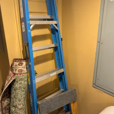 Blue Werner fiberglass stepladder standing alongside a rolled patterned area rug.