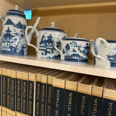 Blue and white ceramic tea set with traditional chinoiserie pagoda landscape pattern, displayed above a vintage set of World Book...