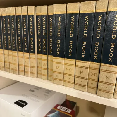 Vintage set of World Book Encyclopedia volumes with cream and navy spines lined up on a bookshelf.