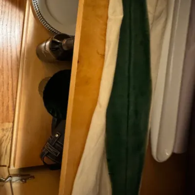 A wooden cabinet shelf filled with mixed kitchen items and linens, including a decorative plate, a glass bottle, and folded towels.