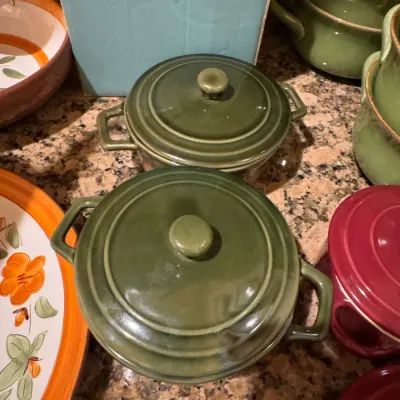 Vintage olive green ceramic covered soup bowls with side handles, surrounded by matching rustic tableware.