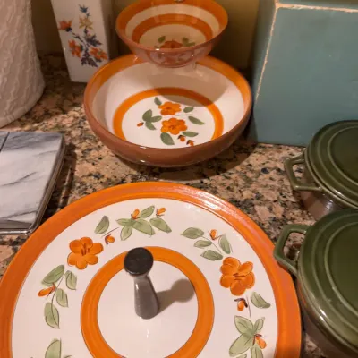 Hand-painted floral ceramic serving ware with orange trim, including a tiered tray, chip-and-dip bowl, and small vase.