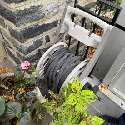 Mobile plastic garden hose reel cart loaded with a dark expandable garden hose, set outdoors near potted plants.