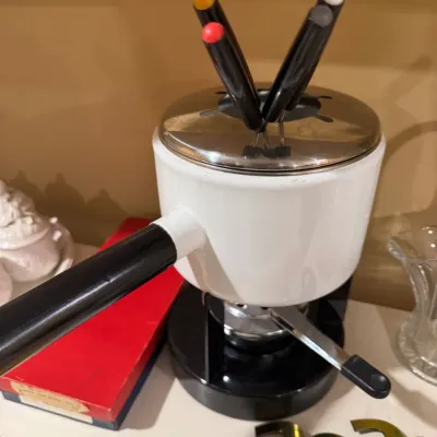 Vintage white enamel fondue pot set with black handle, burner base, stainless steel lid, and color-coded fondue forks.