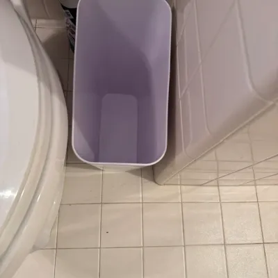Slim modern white plastic trash bin tucked into a bathroom space.