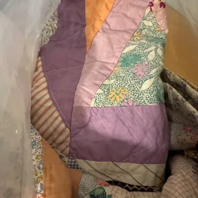 Handmade vintage patchwork quilt featuring a variety of colorful solid, floral, and striped fabric pieces, stored inside clear protective...