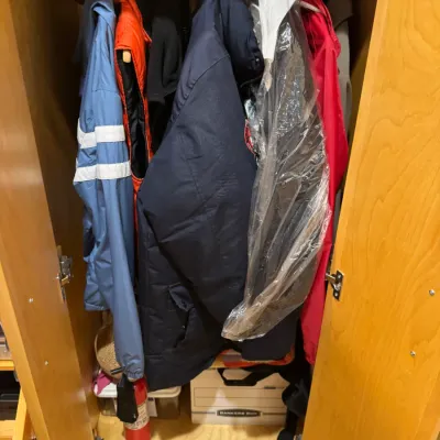 Collection of men's outerwear, including parkas, windbreakers, and a vest, stored inside a wooden armoire closet.