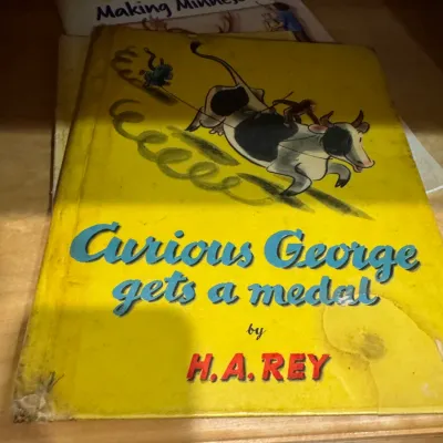 Vintage hardcover edition of 'Curious George Gets a Medal' by H.A. Rey, showing heavy cover wear and edge tear.