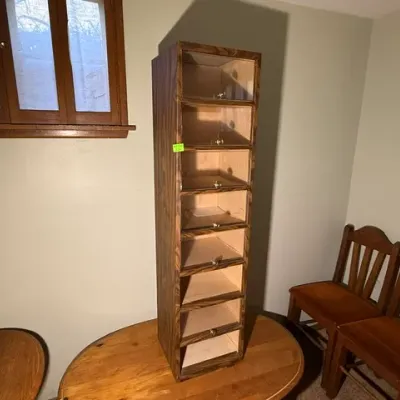 Sale Photo Thumbnail #325: Tall vintage wooden display cabinet with multiple glass-front drop-down compartments, resting on a round wooden dining table.