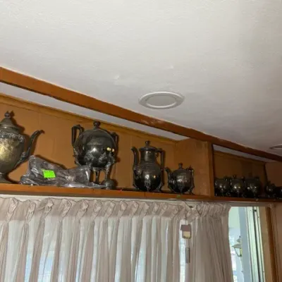 Sale Photo Thumbnail #268: Collection of heavily tarnished silver-plated teapots, coffee pots, and serving pieces displayed on a wooden soffit shelf.