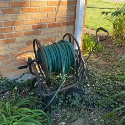 Sale Photo Thumbnail #493: Mobile metal hose reel cart with long handle, featuring a coiled green garden hose, showing light surface wear.