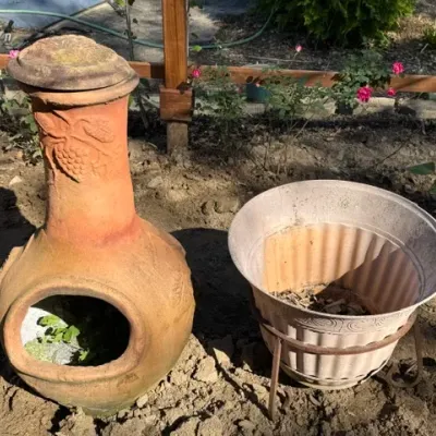 Sale Photo Thumbnail #207: Terracotta chiminea with grape motif detailing alongside a weathered plastic planter set in a metal stand.
