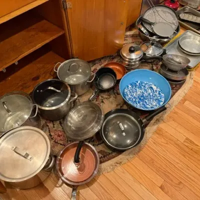 Sale Photo Thumbnail #318: Large assortment of cookware, including stainless steel stockpots, non-stick skillets, baking pans, and a blue speckled enamel bowl, arranged on the floor.