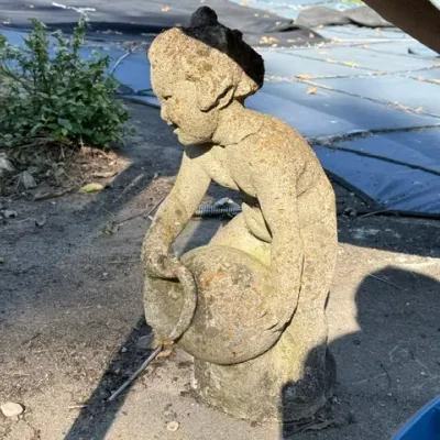 Sale Photo Thumbnail #501: Weathered concrete garden statue depicting a crouching figure holding a vessel, showing significant age, moss growth, and surface wear.