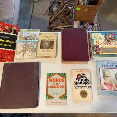 Sale Photo Thumbnail #221: Collection of vintage books, children's storybooks, and stamp albums, including an Illustrated Around-the-World Stamp Album, bags of loose postage stamps, and small wooden display easels.