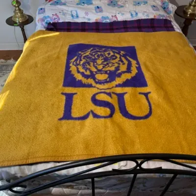 Sale Photo Thumbnail #297: LSU Tigers yellow fleece blanket featuring the classic tiger logo and block lettering, spread across a bed.