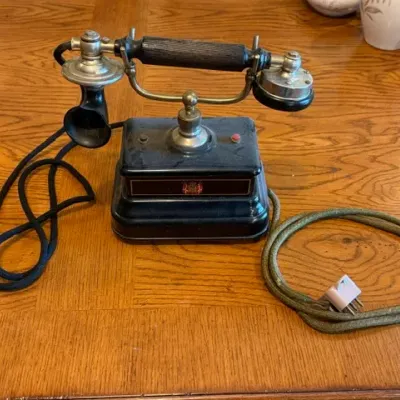 Sale Photo Thumbnail #19: Vintage European cradle desk telephone with a black metal base, brass accents, and a cloth-wrapped cord.