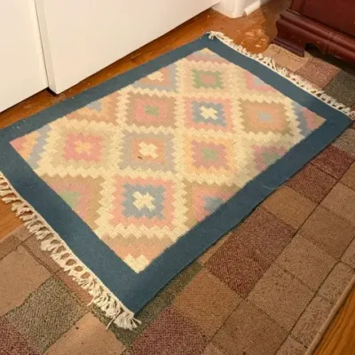 Sale Photo Thumbnail #168: Small pastel geometric flat-weave rug with blue border and fringed ends, displayed on a brown runner.
