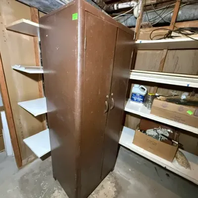 Sale Photo Thumbnail #403: Vintage brown metal storage cabinet with double doors and dual handles, showing surface wear from age.