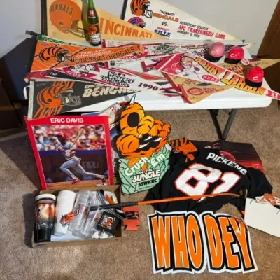Sale Photo Thumbnail #409: Collection of Cincinnati Bengals and Reds sports memorabilia, including vintage felt pennants, an Eric Davis poster, Carl Pickens jersey, mini helmets, and novelty signs from the late 1980s to 1990s.