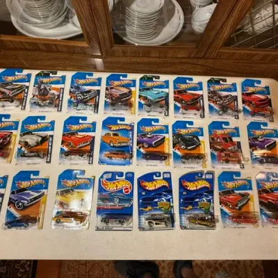 Sale Photo Thumbnail #78: Large collection of 24 carded Mattel Hot Wheels die-cast toy cars arranged on a white table.