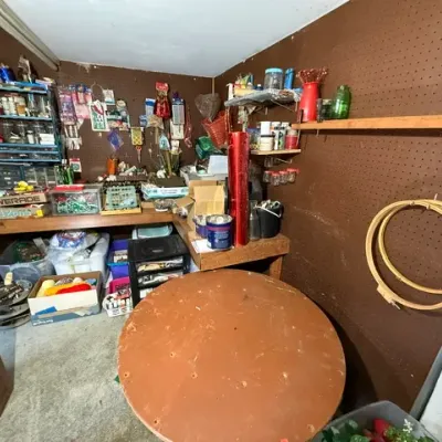 Sale Photo Thumbnail #369: Workshop room filled with assorted crafting supplies, tools, small hardware organizers, and a large round wooden tabletop.