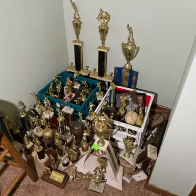 Sale Photo Thumbnail #332: Large collection of vintage youth sports trophies, predominantly featuring baseball figures, displayed on the floor and in crates.