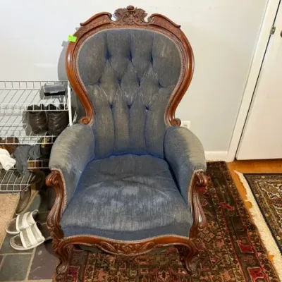 Sale Photo Thumbnail #135: Victorian-style carved wood armchair featuring tufted blue upholstery, ornate crest detailing, and cabriole legs with visible wear to the fabric.