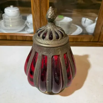 Sale Photo Thumbnail #108: Vintage ruby red blown glass candy jar encased in an ornate pewter or metal filigree frame with a finial lid.
