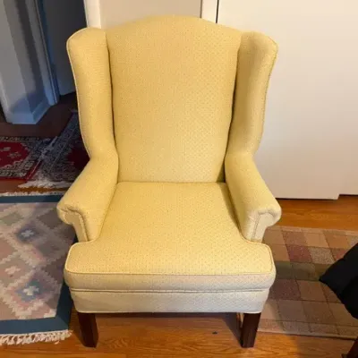 Sale Photo Thumbnail #162: Traditional wingback armchair upholstered in a pale yellow patterned fabric with dark wooden legs.