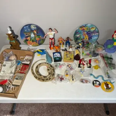 Sale Photo Thumbnail #420: Collection of vintage pop culture toys and memorabilia, including WWF action figures, Scooby-Doo items, Disney figurines, decorative tin plates, and traditional wooden spinning peg tops.