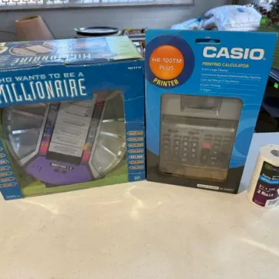 Sale Photo Thumbnail #233: Boxed Who Wants To Be A Millionaire electronic game alongside a boxed Casio HR-100TM Plus printing calculator with paper rolls.