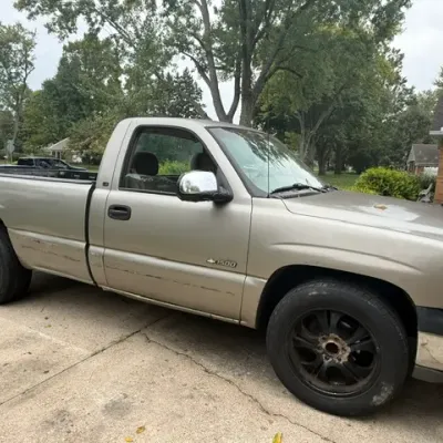 Sale Photo Thumbnail #3: Gold Chevrolet Silverado 1500 regular cab pickup truck with black aftermarket wheels, showing visible wear and scratches along the lower body paneling.