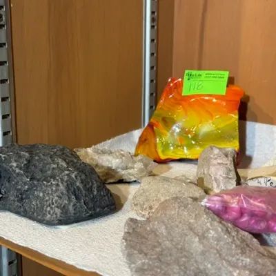 Sale Photo Thumbnail #122: Collection of decorative minerals, rocks, quartz specimens, and a colorful art glass slag piece displayed on a wooden cabinet shelf.