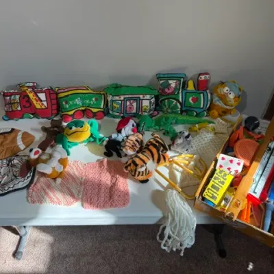 Sale Photo Thumbnail #434: Collection of vintage plush toys, soft fabric train cushions, and miscellaneous play items arranged on a folding table.