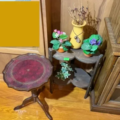 Sale Photo Thumbnail #117: Vintage leather-top pedestal accent table alongside a small three-tier corner plant stand featuring decorative potted artificial flowers and a yellow vase.