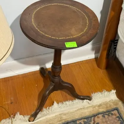 Sale Photo Thumbnail #295: Vintage round wooden side table featuring a gold-embossed leather top, turned pedestal stem, and tripod base.