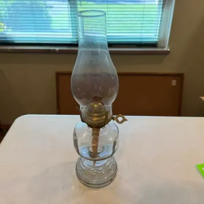 Sale Photo Thumbnail #42: Vintage clear glass kerosene oil lamp featuring a molded glass base, brass burner with wick adjustment key, and a classic glass hurricane shade.