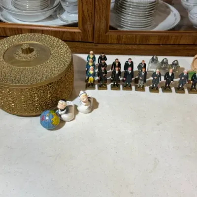 Sale Photo Thumbnail #111: Mid-century textured gold-tone round music box or trinket box displayed alongside miniature figurine collectibles, salt and pepper shakers, and small novelty items.