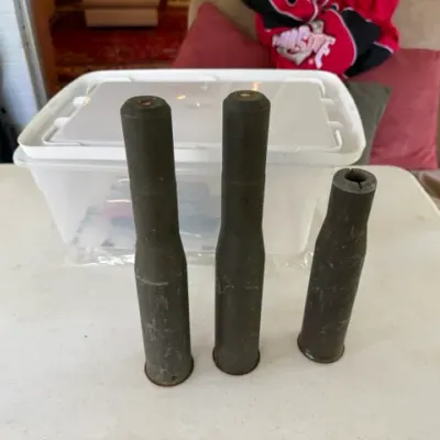 Sale Photo Thumbnail #243: Trio of vintage large-caliber inert artillery or anti-aircraft shell casings showing heavy patina and age-related surface wear.