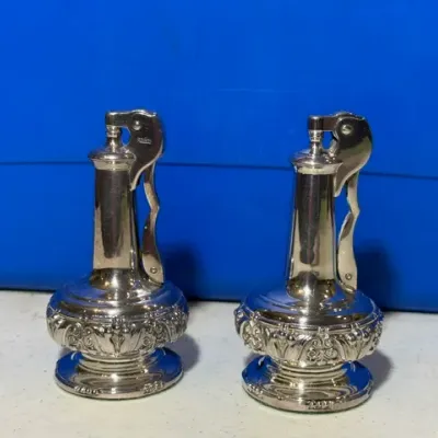 Sale Photo Thumbnail #53: Pair of vintage Ronson silver-plated table lighters featuring ornate repoussé detailing along the weighted bases.
